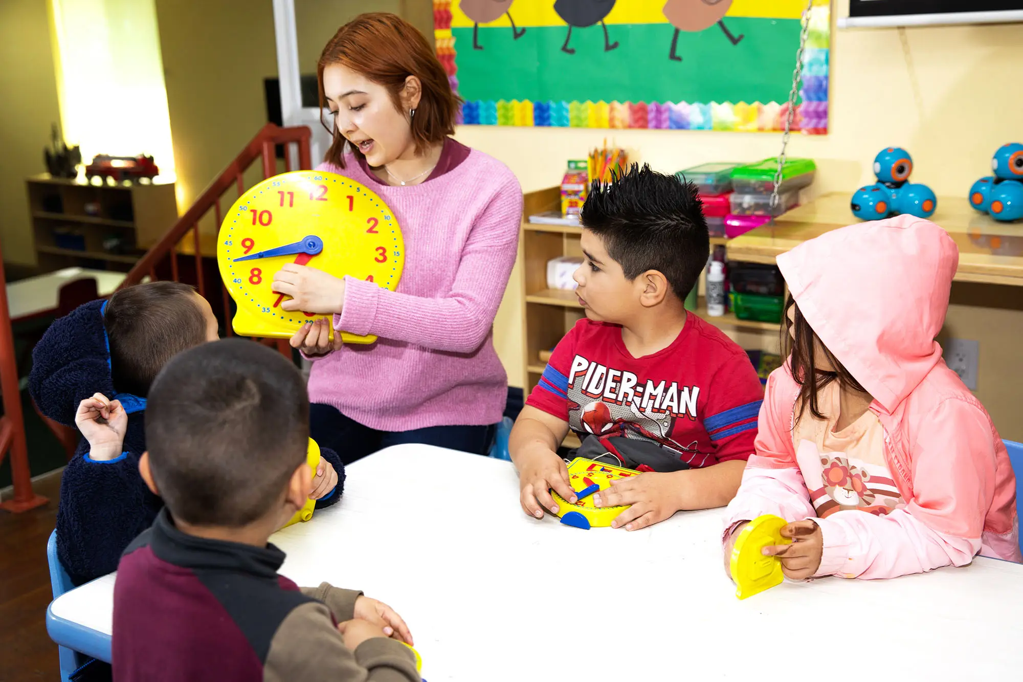 Preschool teacher in Riverside engaged in a guided question-and-answer exchange with a small group of children, the structure that supports language development per MIT research